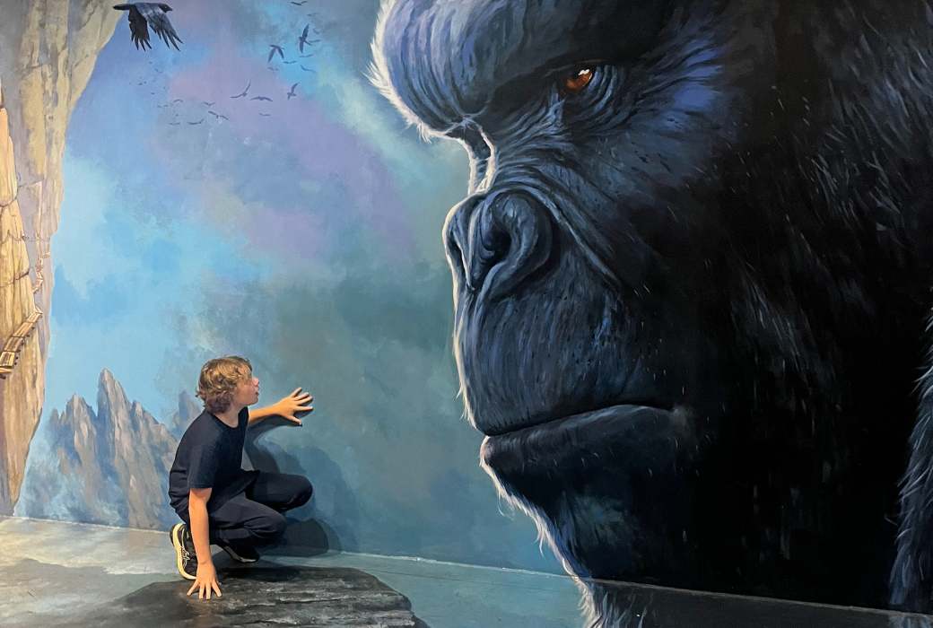 little boy crouching beneath painting of gorilla